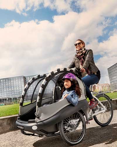 Frau fährt ein Kind im Dreirad Lastenfahrrad