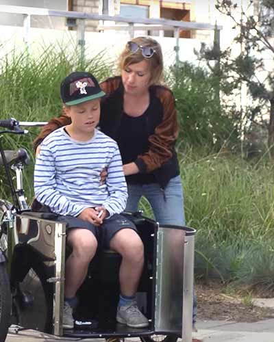 Frau setzt Kind in Dreirad Lastenrad mit Tür vorne