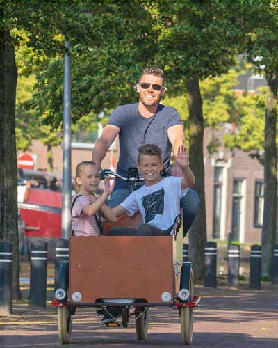 Mann fährt zwei Kinder in Lastenfahrrad Dreirad