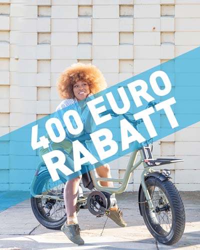 Frau mit Afro sitzt auf kompaktem E Bike. Rabatt 400 Euro