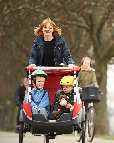 Frau fährt mit Dreirad Lastenrad mit zwei Kindern darin