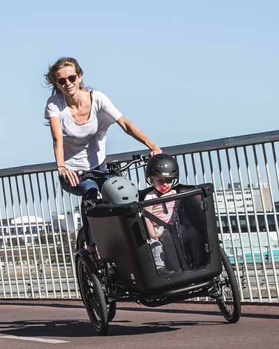 Frau fährt mit zwei Kindern in Dreirad Lastenrad über eine Brücke