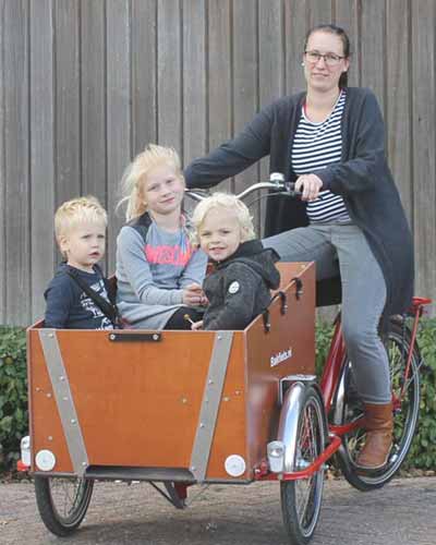 Frau mit drei großen Kindern in Lastenfahrrad mit drei Rädern vorne