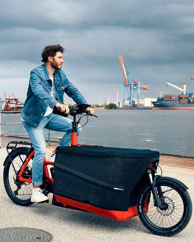 Mann fährt Lastenfahrrad mit großer Kiste vorne durch Hamburger Hafen