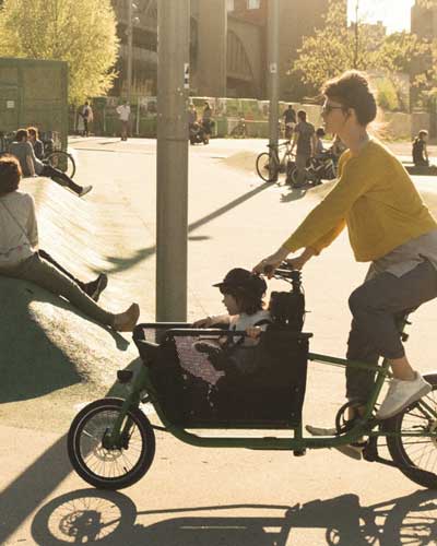 Frau mit kompaktem Lastenrad und einem Kind in der Kiste vorne